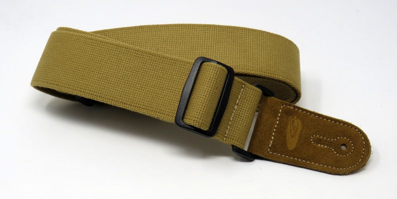 May include: A tan guitar strap with a black adjustable buckle and a brown suede end piece with a logo.