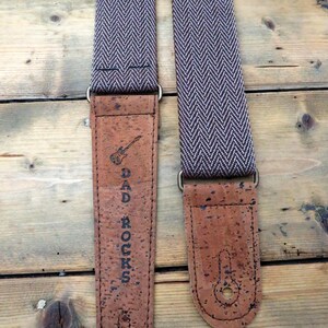 May include: A brown and white guitar strap with a cork end. The cork end has the text "DAD ROCKS" and a small guitar graphic.