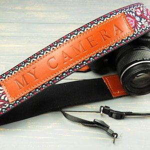 May include: A black camera strap with a colorful floral pattern and a brown leather patch that says "MY CAMERA".