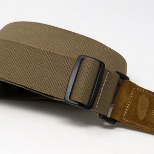 May include: A brown canvas guitar strap with a black adjustable buckle and a brown suede end piece.
