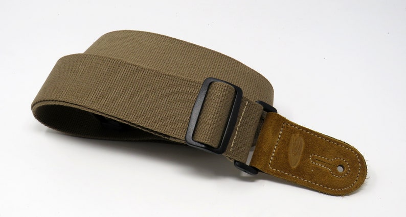 May include: A brown canvas guitar strap with a black adjustable buckle and a brown suede end piece.
