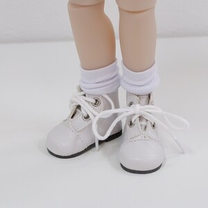 May include: White leather ankle boots with white laces and white socks. The boots have a rounded toe and a lace-up closure.