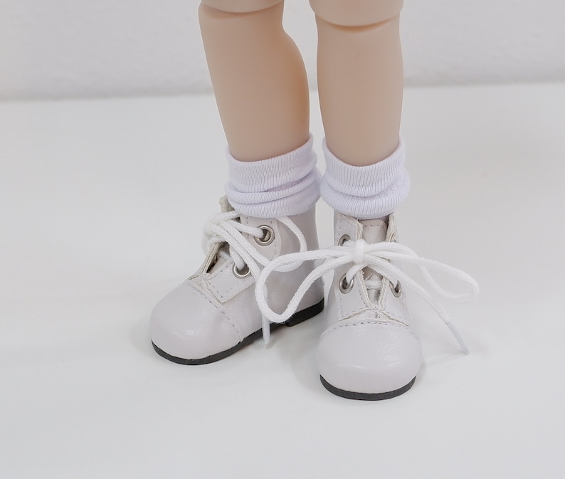 May include: White leather ankle boots with white laces and white socks. The boots have a rounded toe and a lace-up closure.