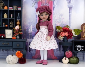 Puede incluir: Muñeca con boina burdeos y vestido con estampado de plumas. La muñeca tiene largas trenzas castañas y lleva zapatos rosas. El fondo incluye un armario azul oscuro, calabazas y un arreglo floral.