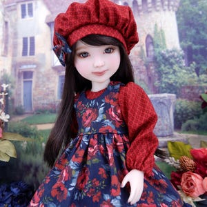 May include: A doll dressed in a red patterned beret and a floral print dress. The dress features a navy blue base with red flowers. The doll has long black hair and is positioned against a blurred garden backdrop.