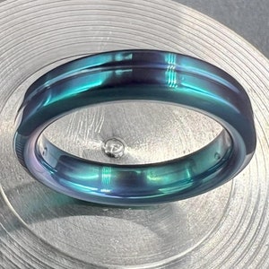 May include: A dark blue and green metal ring with a polished finish. The ring has a beveled edge and a flat top.