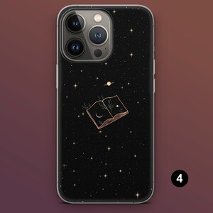Puede incluir: Funda de tel&eacute;fono negra con dise&ntilde;o de noche estrellada. La funda presenta un contorno dorado de un libro abierto con una luna creciente e ilustraciones de plantas. Tambi&eacute;n se representa un planeta y estrellas.
