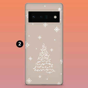 Puede incluir: Una funda de tel&eacute;fono con un dise&ntilde;o festivo. La funda es de color beige claro y presenta un &aacute;rbol de Navidad blanco hecho de luces, junto con copos de nieve y estrellas blancos. La funda tiene un recorte para la c&aacute;mara y el n&uacute;mero "2" en un c&iacute;rculo negro.