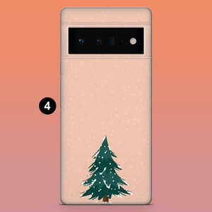 Puede incluir: Una funda de tel&eacute;fono con un tema invernal. La funda tiene un fondo rosa claro con un &aacute;rbol de Navidad verde y puntos de nieve blancos. La funda del tel&eacute;fono tiene una c&aacute;mara y un flash.