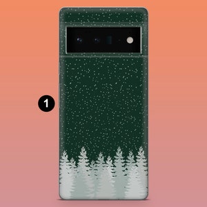 Puede incluir: Funda de tel&eacute;fono verde oscuro con un dise&ntilde;o de bosque invernal. La funda presenta un patr&oacute;n de copos de nieve blancos y una fila de pinos blancos en la parte inferior. La c&aacute;mara y el flash del tel&eacute;fono son visibles en la parte superior.