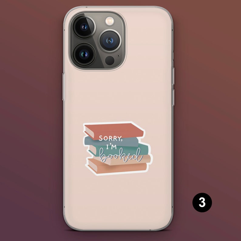 Puede incluir: Funda de tel&eacute;fono rosa claro con una pegatina de una pila de libros. La pegatina tiene el texto "Sorry, I'm booked" en una fuente cursiva. Los libros son en tonos marr&oacute;n, azul y verde.