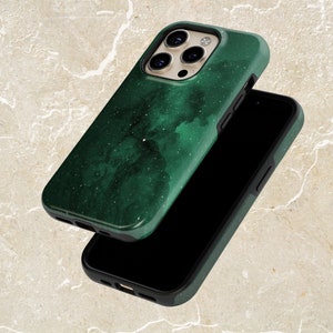 May include: A dark green phone case with a nebula-like design and white speckles. The case is shown with a black smartphone, showcasing the case's protective design and aesthetic appeal. The case has a black border.