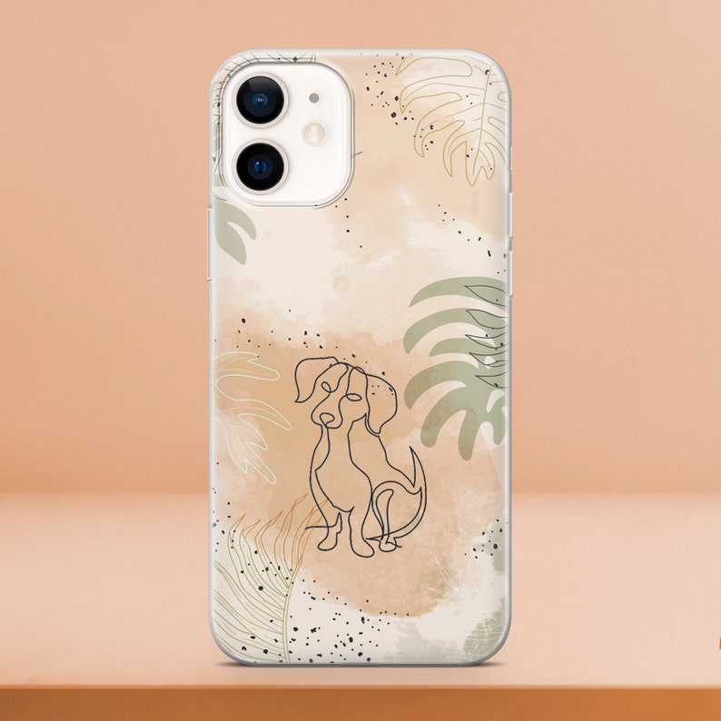 May include: Clear phone case featuring a line drawing of a dog. The design includes watercolor-style beige and brown background with green and white leaf accents. Black speckles add detail to the design.