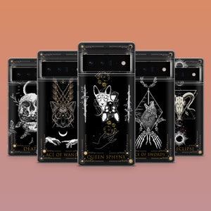 Peut inclure: Coques de téléphone noires avec des motifs de cartes de tarot. Chaque coque présente une illustration différente, notamment un crâne, un loup et un chat. Les coques ont des accents dorés et les noms des cartes de tarot sont imprimés.