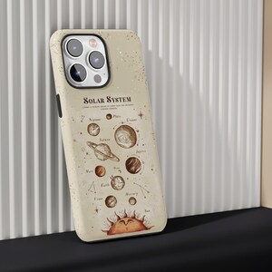 May include: Beige phone case featuring a solar system design with planets and the sun. The case has the text "SOLAR SYSTEM" and a vintage illustration of the planets. The case is leaning against a white ribbed wall.