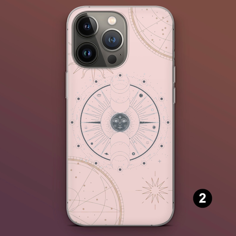 Puede incluir: Una funda de tel&eacute;fono rosa con un dise&ntilde;o celestial que presenta un sol, fases lunares y constelaciones estelares. La funda tiene un borde transparente y un recorte para la c&aacute;mara. El dise&ntilde;o incluye un patr&oacute;n circular con una cara en el centro.