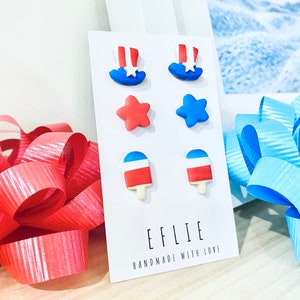 May include: A set of six red, white, and blue polymer clay earrings. The earrings are shaped like stars, ice cream cones, and top hats. The earrings are displayed on a white card with the text "EFLIE HANDMADE WITH LOVE".
