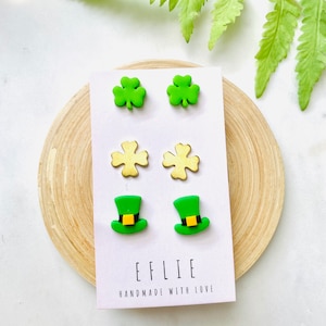 May include: A set of six green and gold shamrock and leprechaun hat earrings. The earrings are displayed on a white card with the text "EFLIE HANDMADE WITH LOVE".