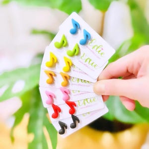 May include: A collection of colorful musical note earrings in various shades, including blue, green, yellow, orange, pink, red, and black. Each pair is displayed on a small white card with the website address www.eflieco.com.