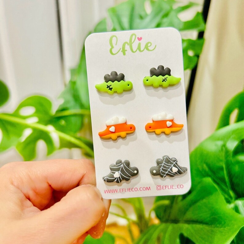 K&ouml;nnte beinhalten: Ein Set aus sechs Halloween-Ohrsteckern auf einer wei&szlig;en Karte. Die Ohrringe zeigen Designs von Frankensteins Monster, Zuckermais und Spinnennetzen. Die Karte hat den Markennamen "Eflie" in gr&uuml;ner Schrift und die Website-Adresse www.eflieco.com.