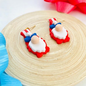 May include: A pair of red, white, and blue gnome earrings. The gnomes are wearing a blue hat with a white star and a white beard.