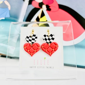 May include: A pair of red heart-shaped earrings with a black and white checkered pattern on top. The earrings are on a white card with the text "EFLIE HAPPY LITTLE THINGS".