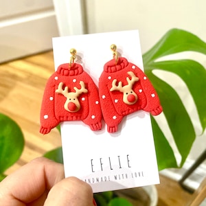Könnte beinhalten: Rote und weiße Weihnachtspullover-Ohrringe mit einem Rentier-Design. Die Ohrringe sind handgefertigt und haben goldene Haken. Die Ohrringe befinden sich auf einer weißen Karte mit dem Text "EFLIE HANDMADE WITH LOVE".