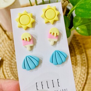 May include: A set of six colorful polymer clay earrings featuring a sun, ice cream, and seashell design. The earrings are displayed on a white card with the text "EFLIE HANDMADE WITH LOVE".