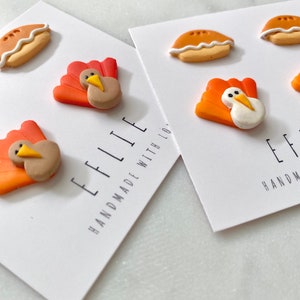 Może przedstawiać: Dwie karty z białym tłem i czarnym tekstem. Tekst na lewej karcie brzmi "Ellie Handmade with Love". Tekst na prawej karcie brzmi "Ellie Handmade with Love". Każda karta ma trzy małe ozdoby z gliny. Ozdoby to indyk, indyk i ciasto.