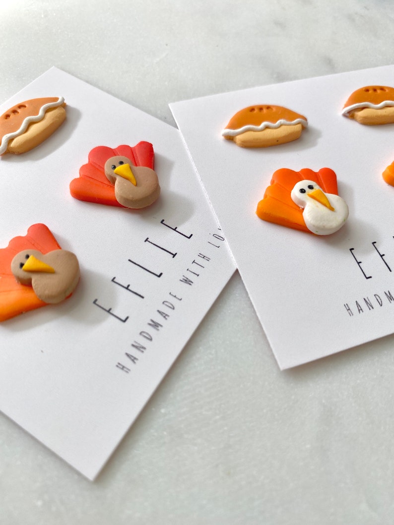 Może przedstawiać: Dwie karty z białym tłem i czarnym tekstem. Tekst na lewej karcie brzmi "Ellie Handmade with Love". Tekst na prawej karcie brzmi "Ellie Handmade with Love". Każda karta ma trzy małe ozdoby z gliny. Ozdoby to indyk, indyk i ciasto.