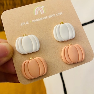 May include: A set of four pumpkin-shaped earrings. Two are white and two are peach. The earrings are handmade and have a gold accent.
