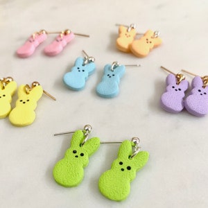May include: A set of pastel-coloured bunny-shaped earrings. The earrings are made of polymer clay and come in yellow, pink, blue, purple, and green.