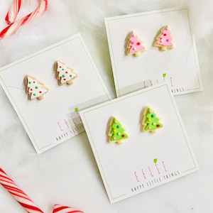 May include: Three sets of Christmas tree-shaped earrings. Each set features a different color frosting: green, pink, and white. The earrings are displayed on white cards with the text "Effie Happy Little Things" printed on them.