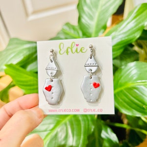 May include: Silver and red heart earrings with a geometric design. The earrings are on a white card with the text "Efie" and website information.