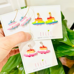 Pode incluir: Três pares de brincos de dinossauro coloridos com um coração no topo. Os brincos estão em um cartão branco com o texto "EFFLIE HAPPY LITTLE THINGS".