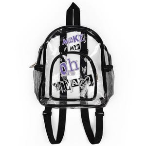 Puede incluir: Mochila transparente con rayas verticales blancas y negras y ribetes negros. La mochila tiene las palabras "MAKE ME!" y "oh YEAH?" en letras moradas y negras. Cuenta con correas negras para los hombros y bolsillos laterales de malla.