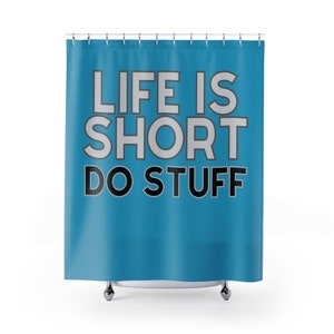 Puede incluir: Cortina de ducha turquesa con el texto "LIFE IS SHORT DO STUFF" en negrita, fuente sans-serif. El texto es blanco con un contorno gris. La cortina cuelga de una barra de metal con ganchos plateados.