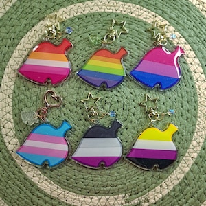 Könnte beinhalten: Sechs verschiedene farbige, blattartige Anhänger mit einem Stern- und Herzdesign. Die Anhänger sind aus klarem Acryl gefertigt und haben verschiedene Farben und Streifen. Die Anhänger sind an einer goldenen Kette befestigt.