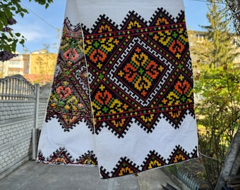 May include: White fabric with a black, red, yellow, and green embroidered design. The design features geometric shapes and floral motifs.