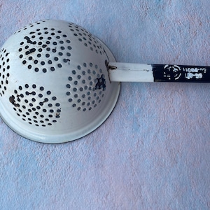 May include: White enamel colander with a black handle. The handle has the text "Made in USA" printed on it.