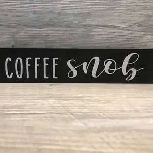 May include: Black wooden sign with the text "COFFEE SNOB" in white lettering.
