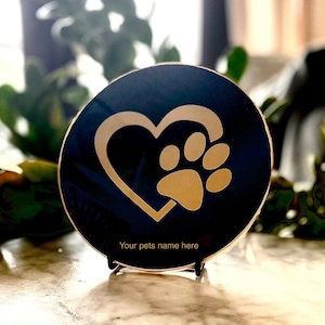 May include: A black round plaque with a gold heart and paw print design. The plaque has the text "Your pets name here" on the bottom.