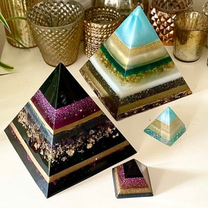 May include: Four resin pyramids in various sizes and colors. The largest pyramid is blue and white with gold accents. The second largest pyramid is black with gold and purple accents. The smallest pyramid is blue and white with gold accents. The fourth pyramid is black with gold and purple accents.