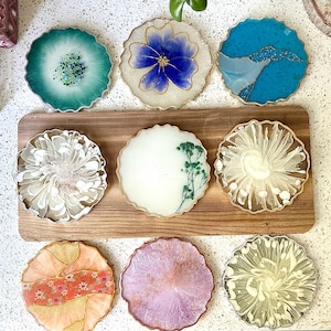 May include: Set of 9 resin coasters with various designs, including floral, abstract, and geometric patterns. The coasters are round and have a white, gold, and blue color scheme.
