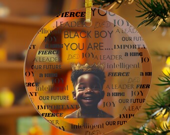 May include: A round glass ornament with a black and white photo of a young boy wearing a gold crown. The ornament is decorated with the words "Black Boy You Are... Important, Fierce, A Leader, A King, Intelligent, Loved, Joy" repeated around the image.