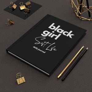 May include: Black journal with the text "black girl soft life" and "daily journal" in white lettering.