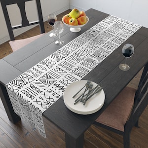 May include: Black and white geometric patterned table runner on a dark wood table with white plates and silverware.