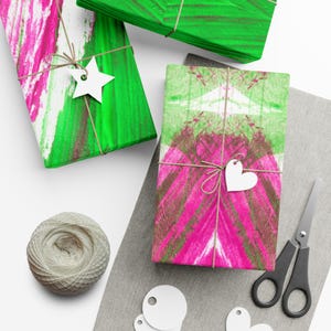 May include: Overhead view of wrapped presents with abstract pink and green brushstroke designs. Each package is tied with twine and a white paper tag. A ball of twine, scissors, and additional tags are also visible.