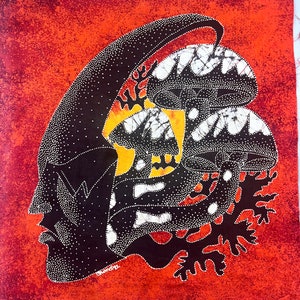 May include: A batik wall hanging with a black and white silhouette of a face and mushrooms on an orange background. The mushrooms have white and black patterns and are surrounded by black and white foliage. The artist's signature "Chandra" is in the bottom left corner.