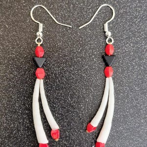 Peut inclure: Une paire de boucles d'oreilles pendantes avec des perles blanches, rouges et noires. Les boucles d'oreilles ont une fermeture à crochet argentée.